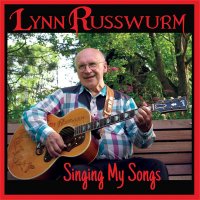 CD cover art ~ Lynn Russwurm sitting on a bench playing his woodburned guitar